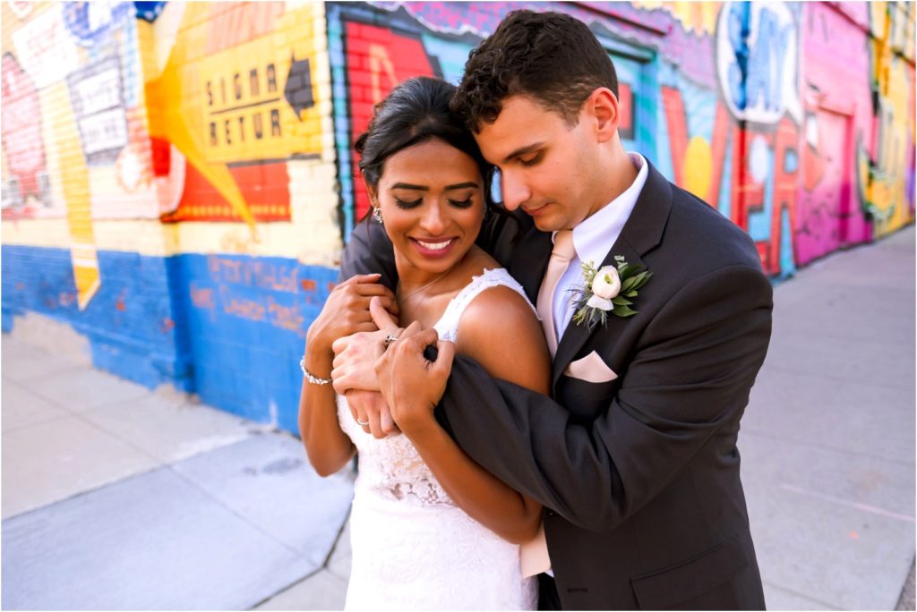 Photo of a groom holding his bride from behind in front of a colorful mural in Eastern Market Detroit